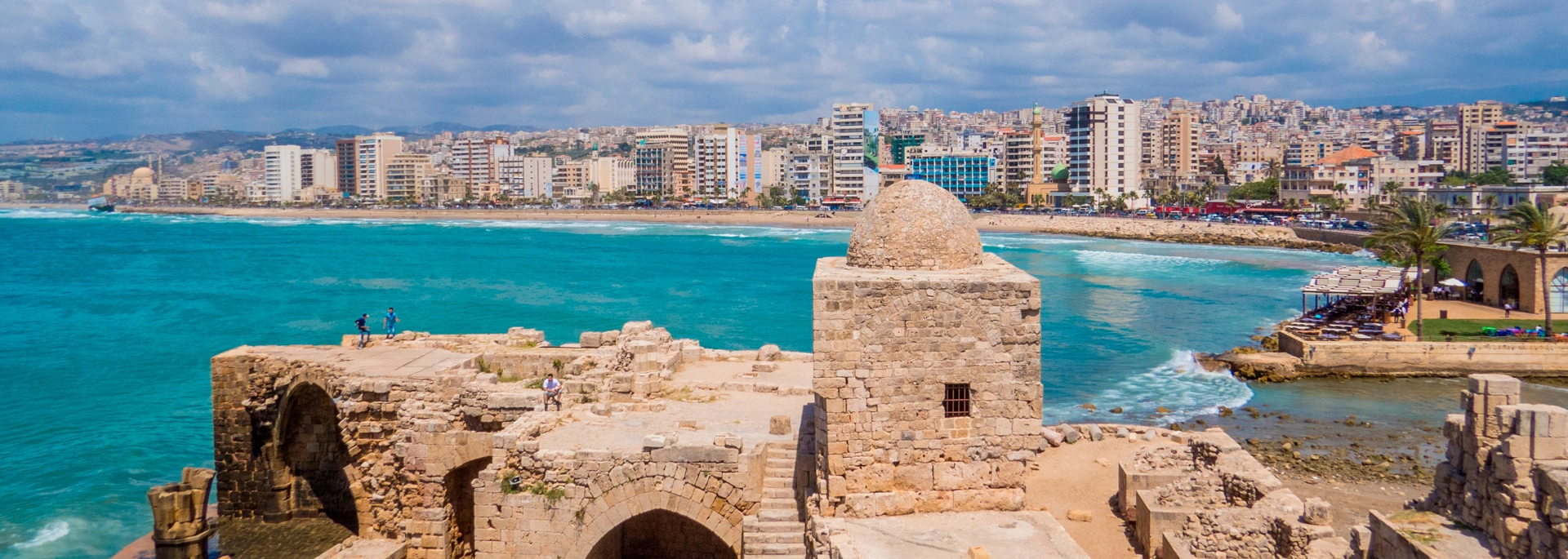  View of Sidon’s historic Sea Castle on the Mediterranean coast, with turquoise waters in the foreground and the modern city skyline in the background under a partly cloudy sky